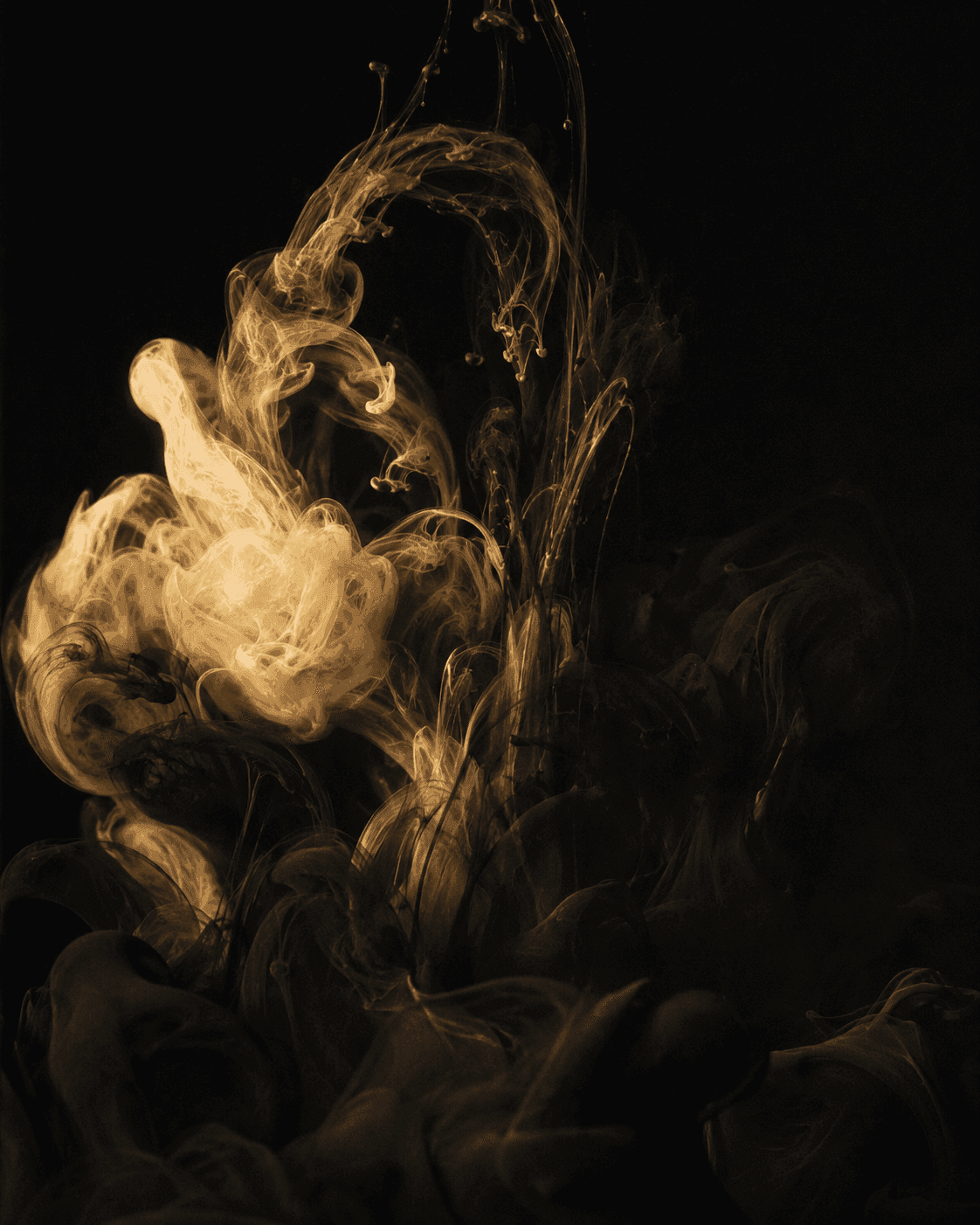 A plume of golden ink blooming and unfurling through darkness.